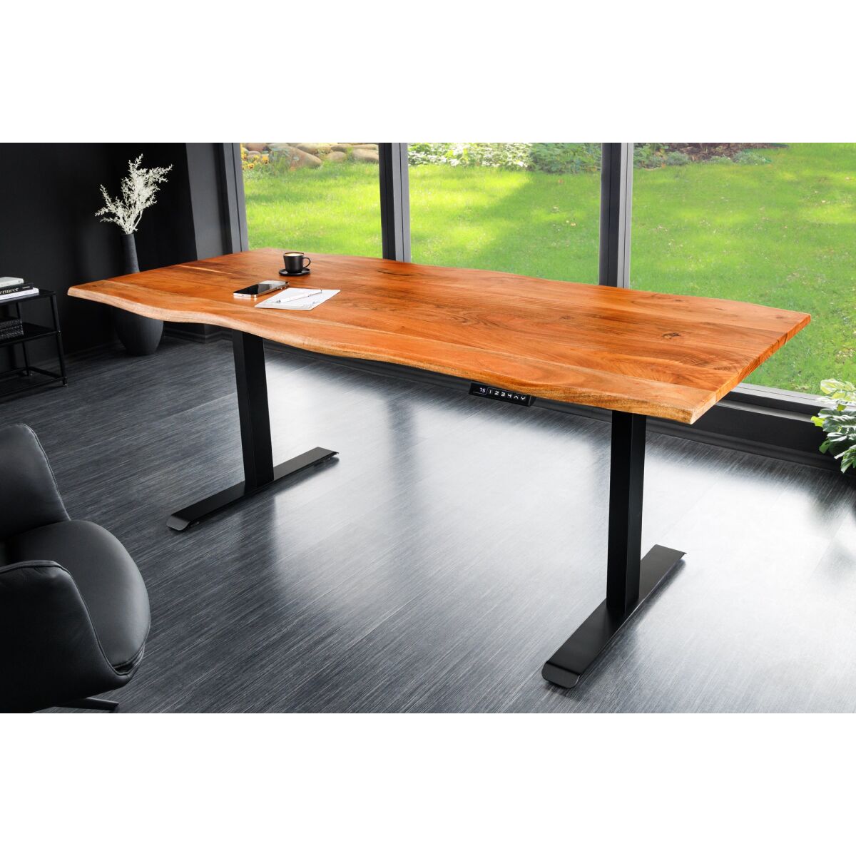 Wooden live edge electric adjustable office table with black legs in a room with large windows showing greenery